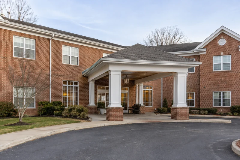 Covered entrance to a two-story brick senior living facility, minimal landscaping
